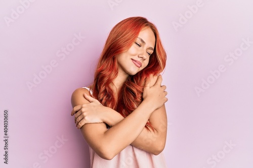 Young beautiful redhead woman wearing casual clothes over pink background hugging oneself happy and positive  smiling confident. self love and self care