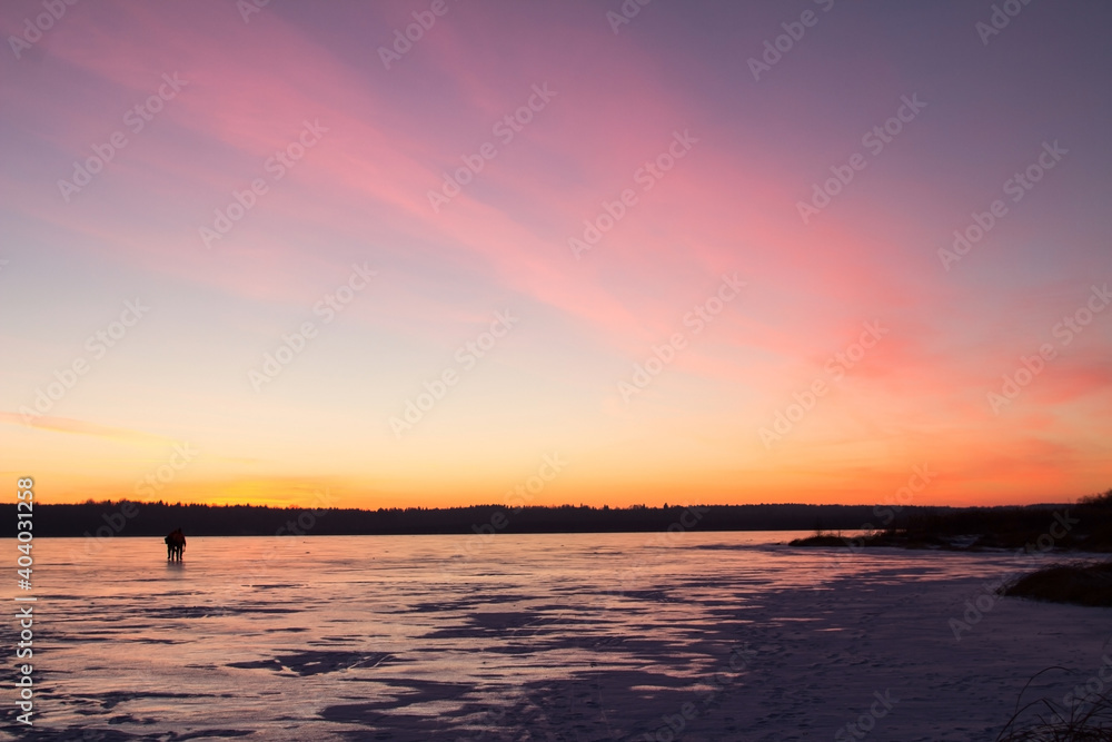 Two silhouettes of people against the background of the sunset on the ice of a frozen lake. Winter background. Copy Space