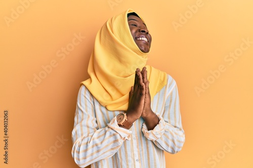 Beautiful african young woman wearing traditional islamic hijab scarf begging and praying with hands together with hope expression on face very emotional and worried. begging. © Krakenimages.com