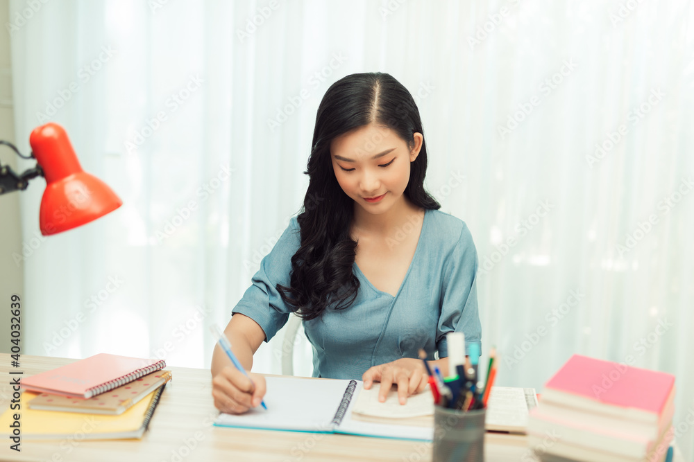Teen girl preparing for test exam with laptop and books writing essay coursework in notebook studying at home Teen girl preparing for test exam with laptop and books writing essay coursework in notebook studying at home