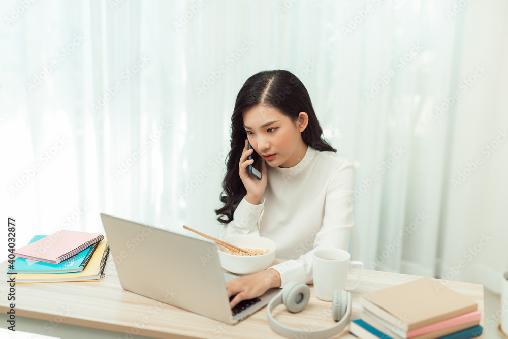 woman eating noodles while working with laptop and cellphone in office woman eating noodles while working with laptop and cellphone in office
