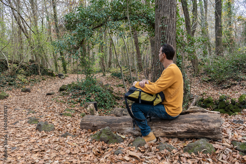 Man sitting with backpack on woods looking horizon in forest.Stylish hiker outdoor lifestyle.Travel wanderlust concept.Copy space . Man sitting with backpack on woods looking horizon in forest.Stylish hiker outdoor lifestyle.Travel wanderlust concept.Copy space .