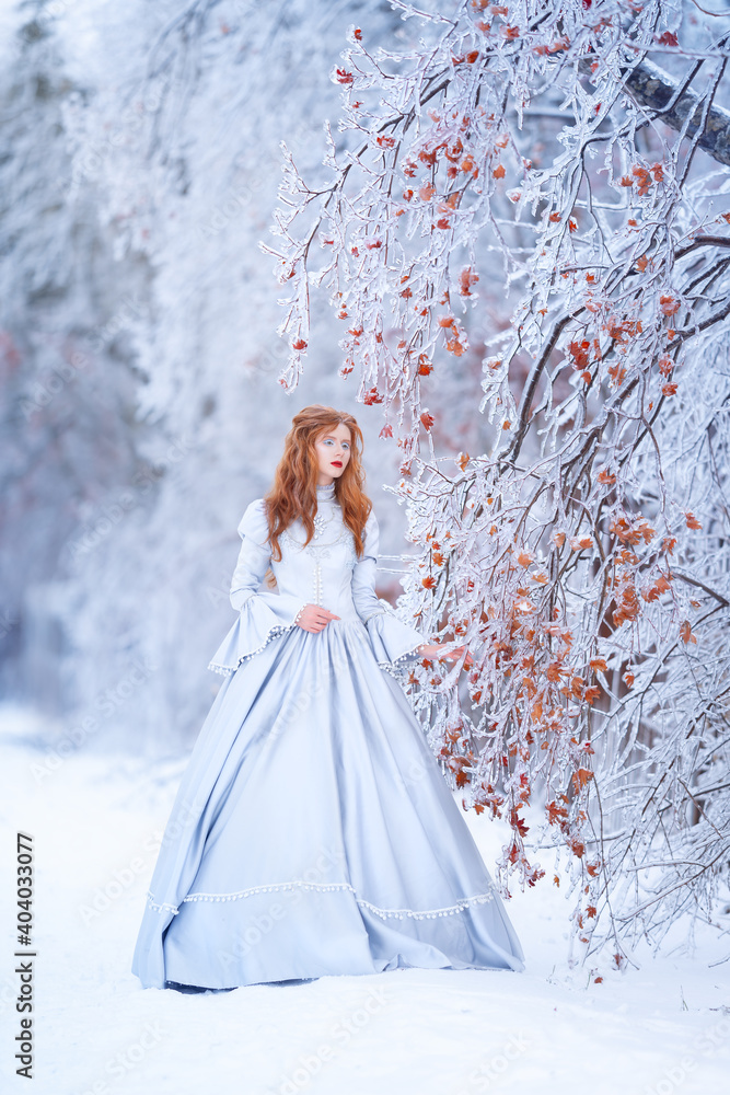 Young redhead woman, a princess, walks in a winter forest in a blue dress. Young redhead woman, a princess, walks in a winter forest in a blue dress.