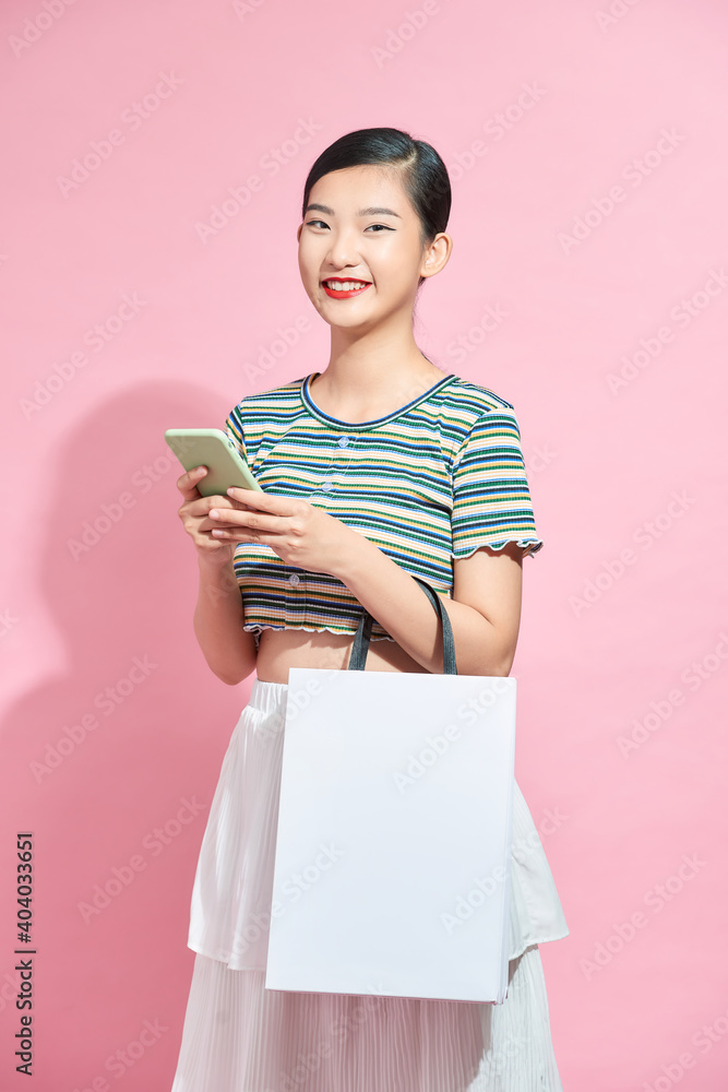 Trendy beautiful young Asian woman carrying colorful bags shopping online with mobile phone isolated on pink background Trendy beautiful young Asian woman carrying colorful bags shopping online with mobile phone isolated on pink background