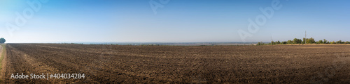 Panorama. Autumn landscape, black empty field after harvest on blue sky background