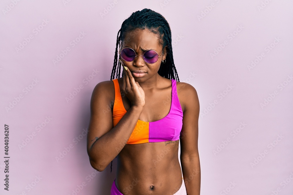 Young african american woman wearing bikini and sunglasses touching mouth with hand with painful expression because of toothache or dental illness on teeth. dentist Young african american woman wearing bikini and sunglasses touching mouth with hand with painful expression because of toothache or dental illness on teeth. dentist