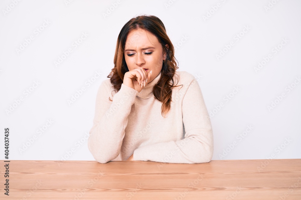 Young beautiful caucasian woman wearing turtleneck sweater sitting on the table feeling unwell and coughing as symptom for cold or bronchitis. health care concept. Young beautiful caucasian woman wearing turtleneck sweater sitting on the table feeling unwell and coughing as symptom for cold or bronchitis. health care concept.