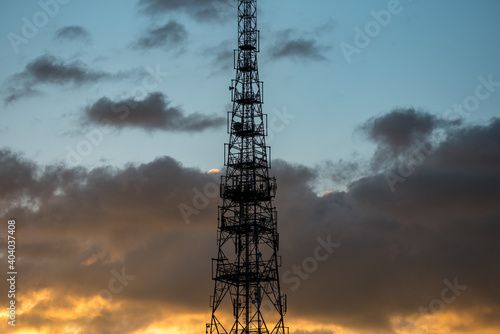 Cell phone relay tower. The construction of the mast against the blue sky and clouds illuminated by the yellow light of the setting sun.