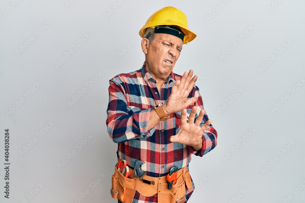 Senior hispanic man wearing handyman uniform disgusted expression, displeased and fearful doing disgust face because aversion reaction. with hands raised Senior hispanic man wearing handyman uniform disgusted expression, displeased and fearful doing disgust face because aversion reaction. with hands raised