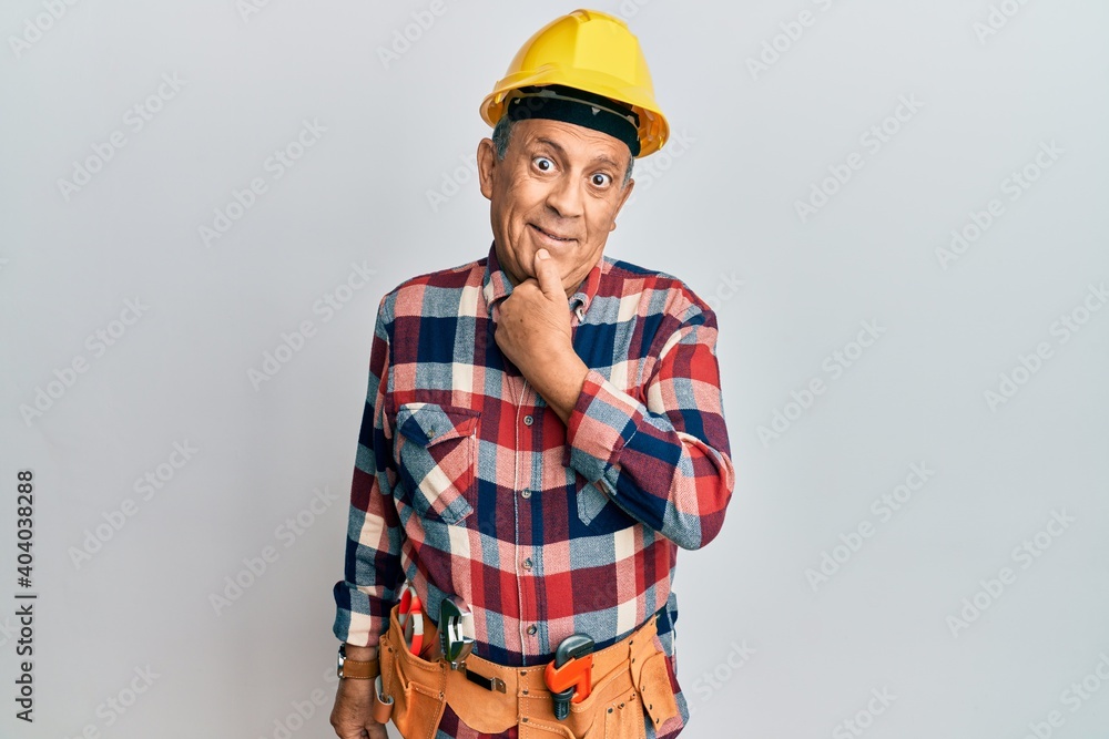 Senior hispanic man wearing handyman uniform looking confident at the camera with smile with crossed arms and hand raised on chin. thinking positive.