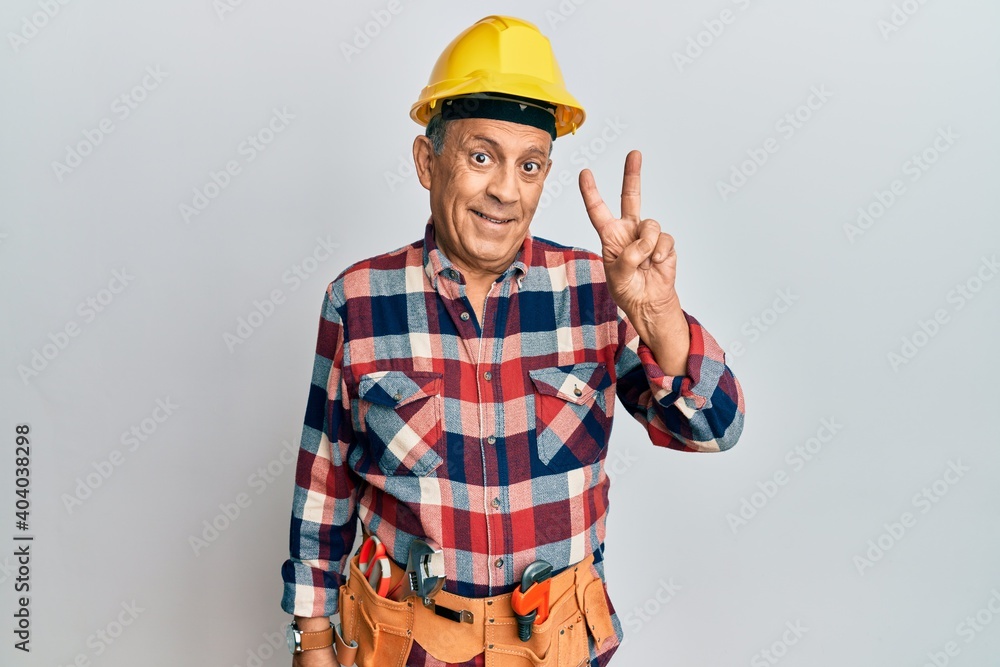 Senior hispanic man wearing handyman uniform showing and pointing up with fingers number two while smiling confident and happy. Senior hispanic man wearing handyman uniform showing and pointing up with fingers number two while smiling confident and happy.