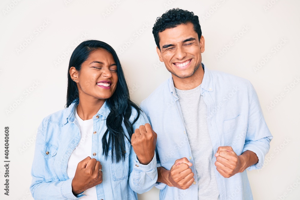 Beautiful latin young couple wearing casual clothes excited for success with arms raised and eyes closed celebrating victory smiling. winner concept. Beautiful latin young couple wearing casual clothes excited for success with arms raised and eyes closed celebrating victory smiling. winner concept.