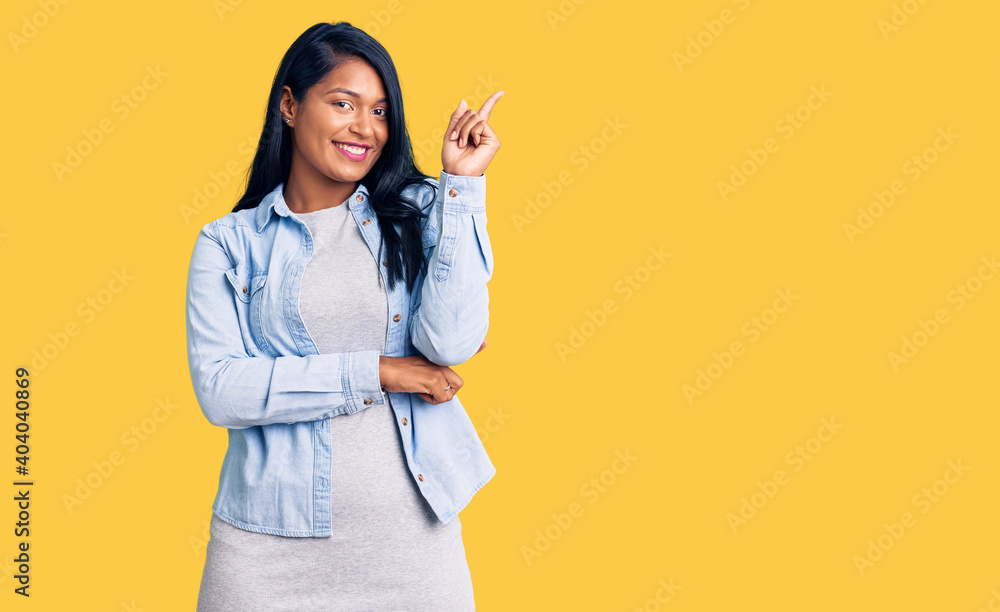 Hispanic woman with long hair wearing casual denim jacket with a big smile on face, pointing with hand and finger to the side looking at the camera. Hispanic woman with long hair wearing casual denim jacket with a big smile on face, pointing with hand and finger to the side looking at the camera.