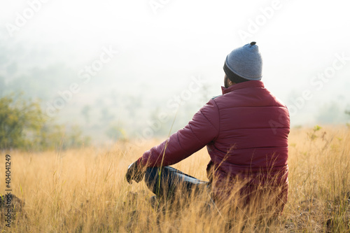Back view of traveller meditating on top of the mountain during cold fogy morning sunrise - Concept of connecting with nature, enlightenment and mindfulness.