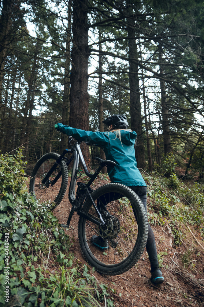 Cyclist girl with mountain bike ascending mtb trail in forest