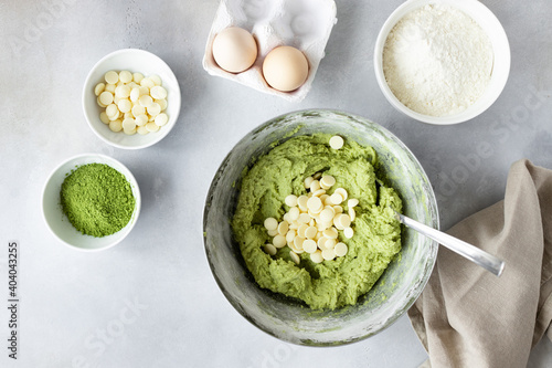 Flat lay composition with green tea matcha dough in bowl, white chocolate chips, eggs, flour on a gray background. Healthy nutrition, superfoods. place for text.