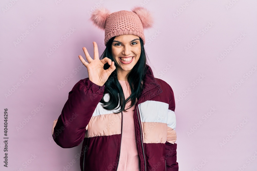 Young hispanic woman wearing wool winter sweater and cap smiling positive doing ok sign with hand and fingers. successful expression. Young hispanic woman wearing wool winter sweater and cap smiling positive doing ok sign with hand and fingers. successful expression.