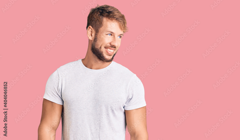 Fototapeta premium Young caucasian man wearing casual white tshirt looking away to side with smile on face, natural expression. laughing confident.