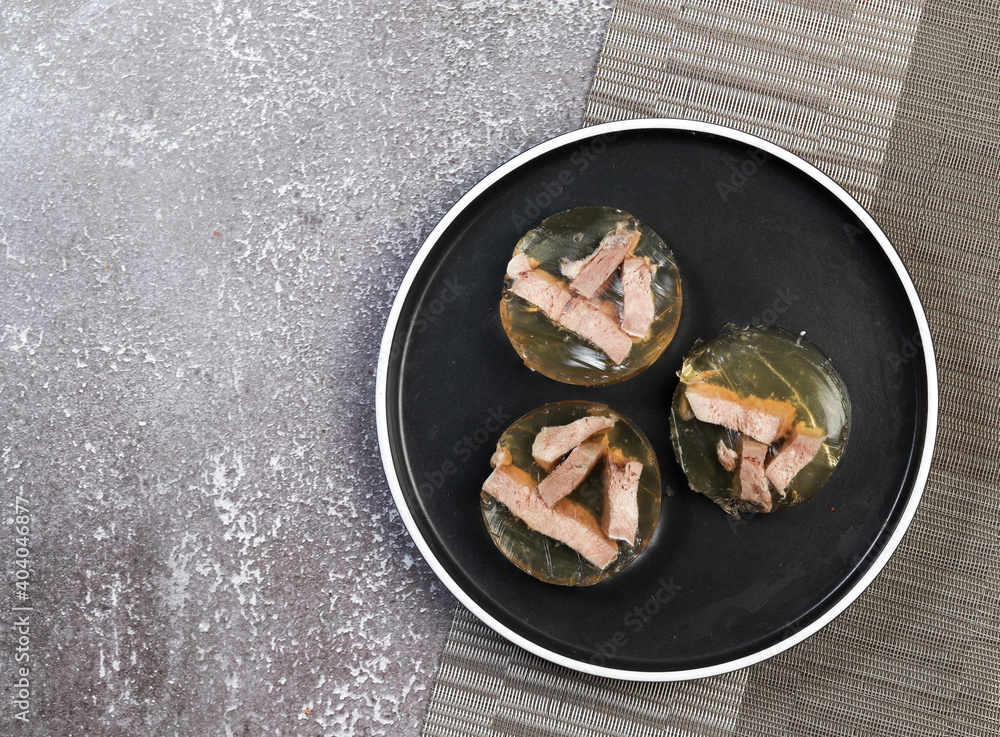 Aspic jellied meat on a round plate on a dark background. Top view, flat lay Aspic jellied meat on a round plate on a dark background. Top view, flat lay