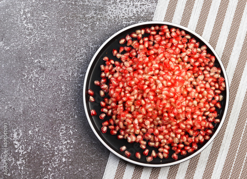 Pomegranate seeds on a round plate on a dark background. Top view, flat lay