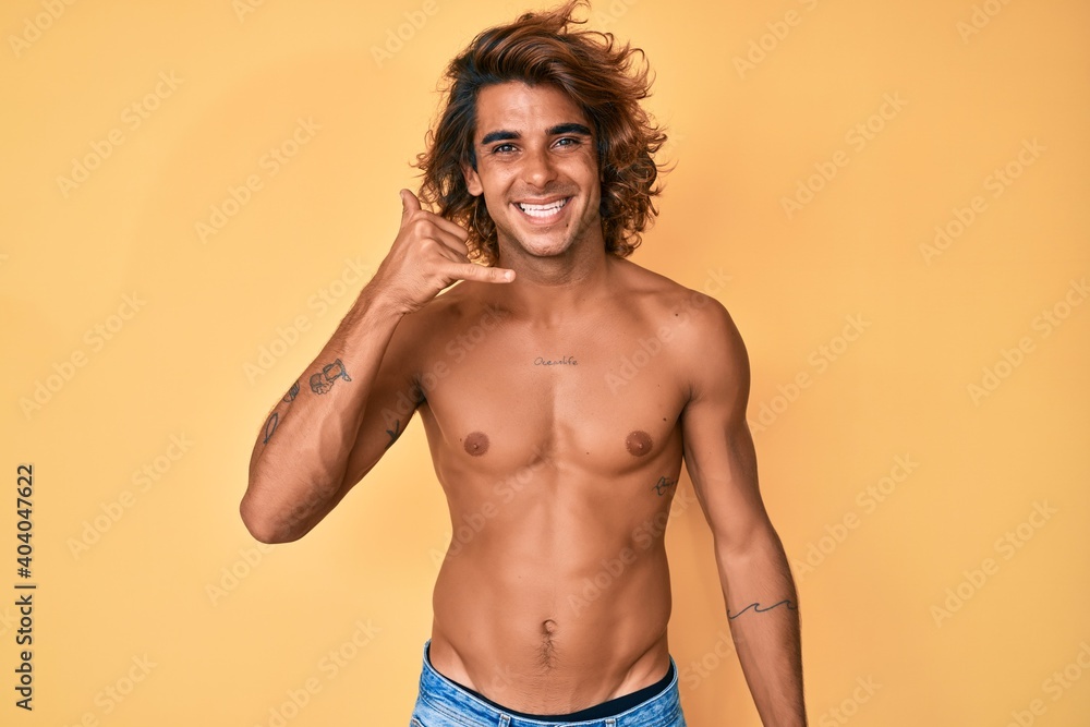 Young hispanic man standing shirtless smiling doing phone gesture with hand and fingers like talking on the telephone. communicating concepts.