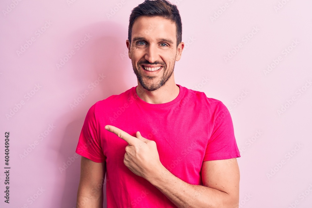 Young handsome man wearing casual t-shirt standing over isolated pink background smiling cheerful pointing with hand and finger up to the side Young handsome man wearing casual t-shirt standing over isolated pink background smiling cheerful pointing with hand and finger up to the side