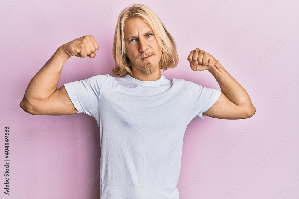 Caucasian young man with long hair wearing casual white t shirt showing arms muscles smiling proud. fitness concept. Caucasian young man with long hair wearing casual white t shirt showing arms muscles smiling proud. fitness concept.