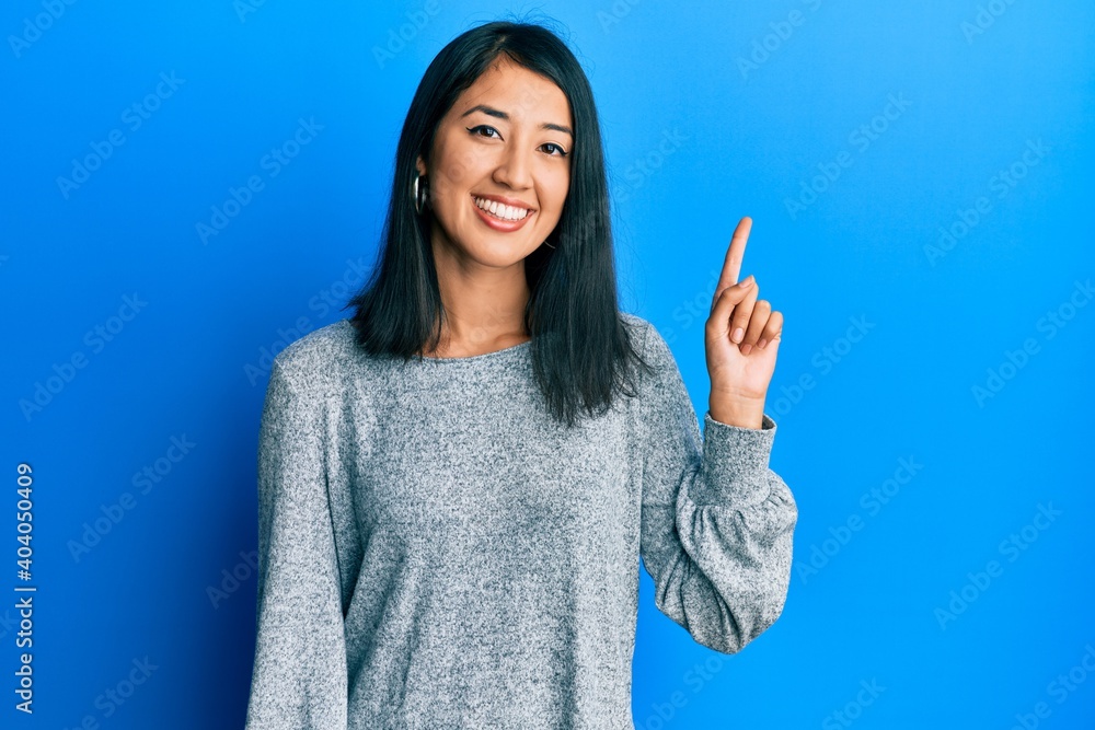 Beautiful asian young woman wearing casual clothes smiling with an idea or question pointing finger up with happy face, number one Beautiful asian young woman wearing casual clothes smiling with an idea or question pointing finger up with happy face, number one