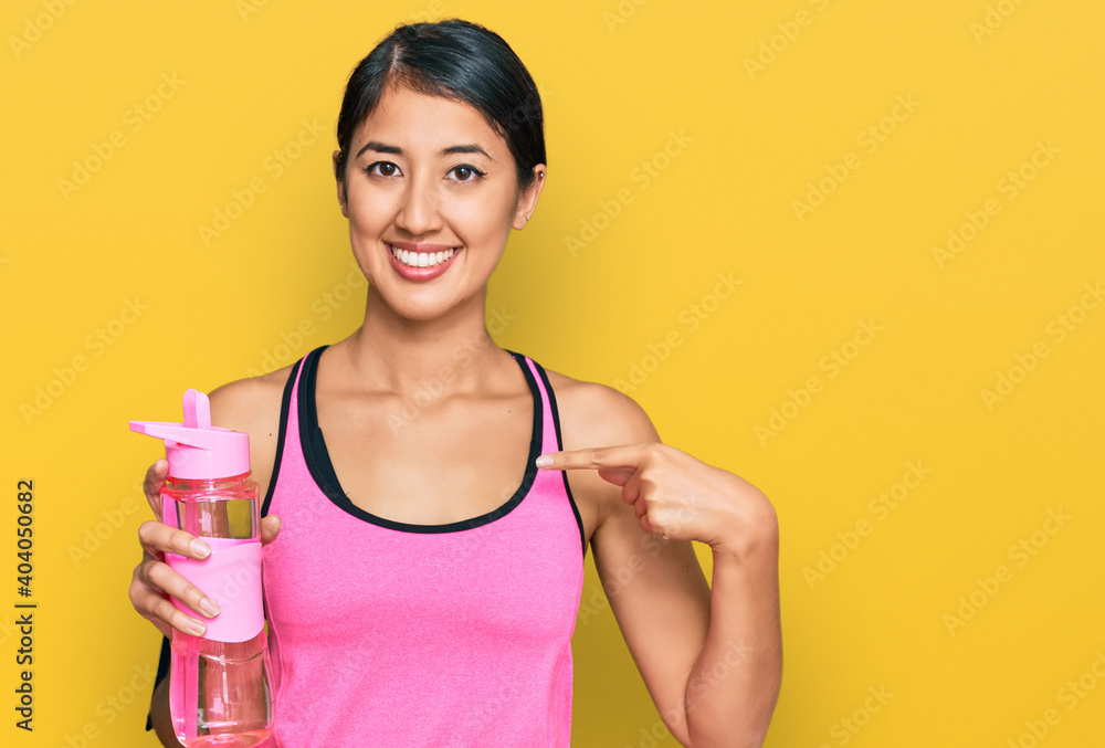 Beautiful asian young sport woman wearing sportswear drinking bottle of water pointing finger to one self smiling happy and proud Beautiful asian young sport woman wearing sportswear drinking bottle of water pointing finger to one self smiling happy and proud
