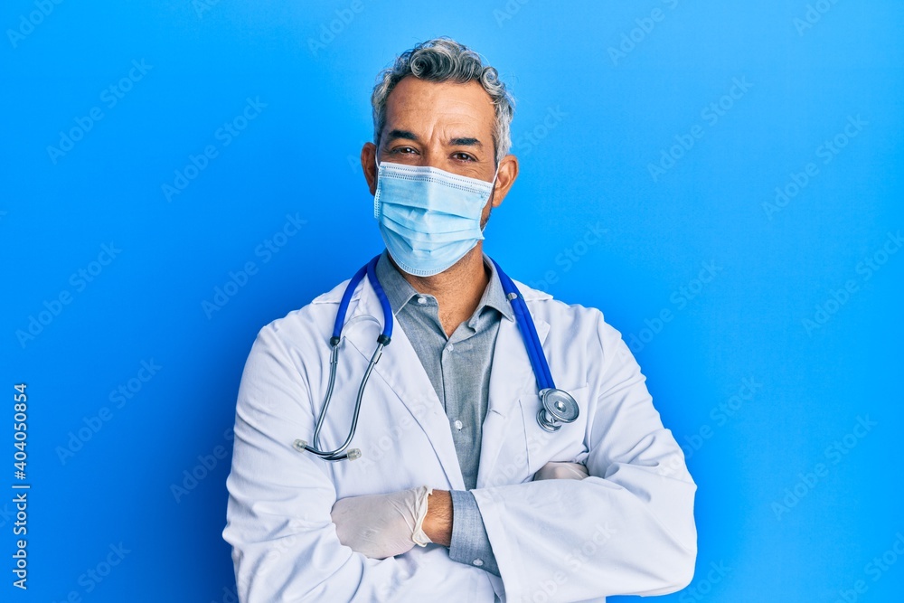 Middle age grey-haired man wearing doctor uniform and medical mask happy face smiling with crossed arms looking at the camera. positive person. Middle age grey-haired man wearing doctor uniform and medical mask happy face smiling with crossed arms looking at the camera. positive person.