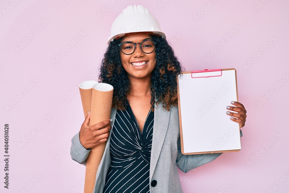 Young african american woman wearing architect hardhat holding blueprints and clipboard smiling with a happy and cool smile on face. showing teeth. Young african american woman wearing architect hardhat holding blueprints and clipboard smiling with a happy and cool smile on face. showing teeth.