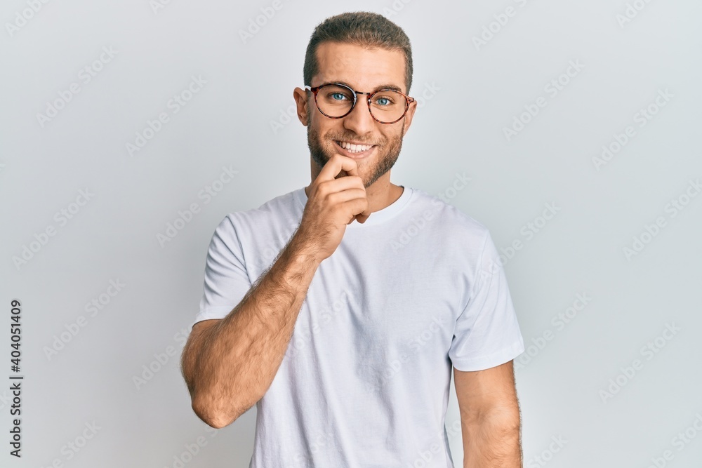 Young caucasian man wearing casual clothes and glasses looking confident at the camera with smile with crossed arms and hand raised on chin. thinking positive. Young caucasian man wearing casual clothes and glasses looking confident at the camera with smile with crossed arms and hand raised on chin. thinking positive.