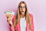 Young blonde woman wearing business style holding 50 euro banknotes scared and amazed with open mouth for surprise, disbelief face