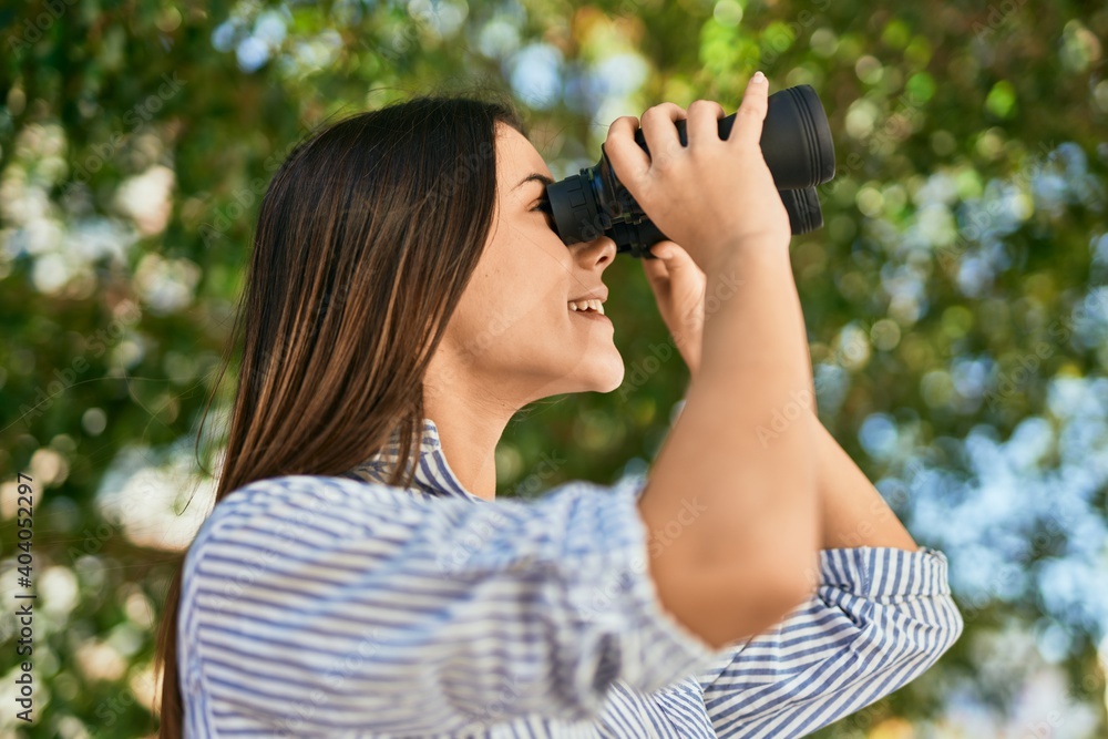 Young hispanic girl smiling happy using binoculars at the park.