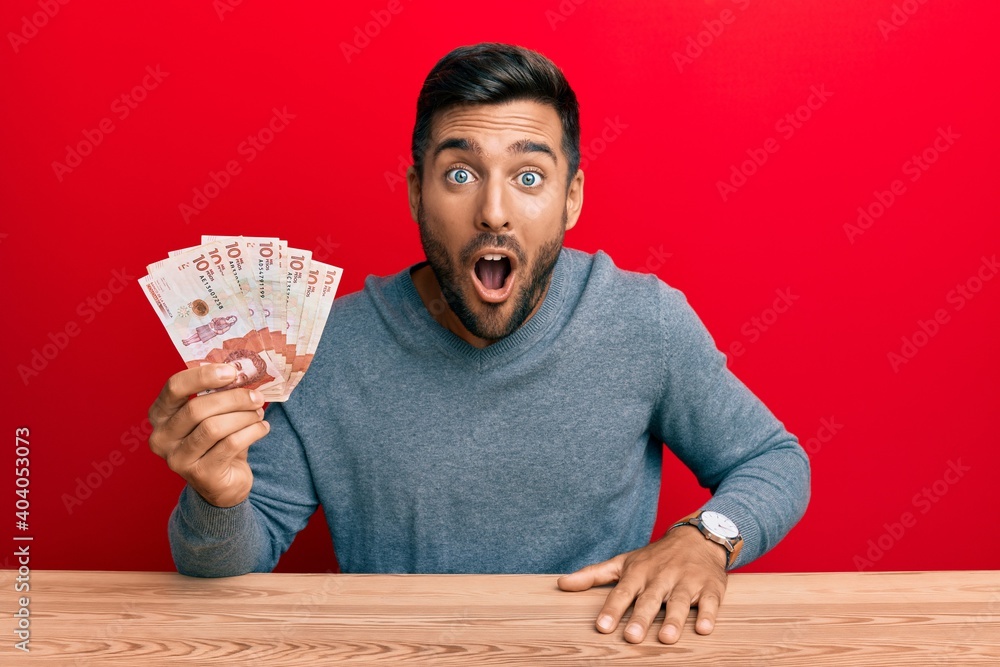 Handsome hispanic man holding colombian pesos scared and amazed with open mouth for surprise, disbelief face Handsome hispanic man holding colombian pesos scared and amazed with open mouth for surprise, disbelief face
