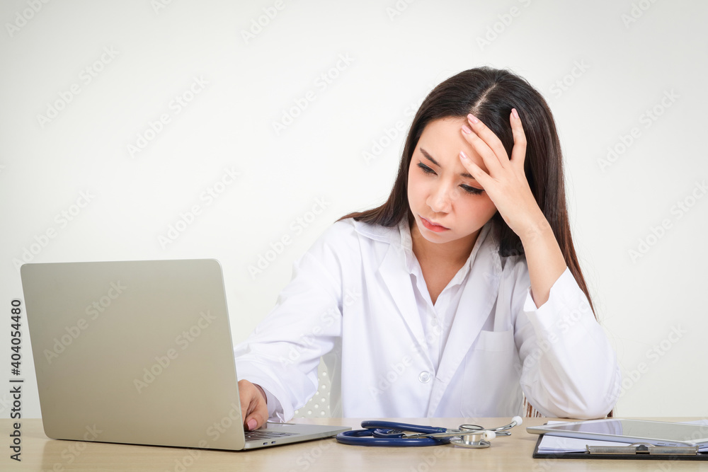 An Asian woman doctor in uniform works with a laptop There is cumulative stress, overwork, and stress caused by the coronavirus that spread throughout the world. White background An Asian woman doctor in uniform works with a laptop There is cumulative stress, overwork, and stress caused by the coronavirus that spread throughout the world. White background