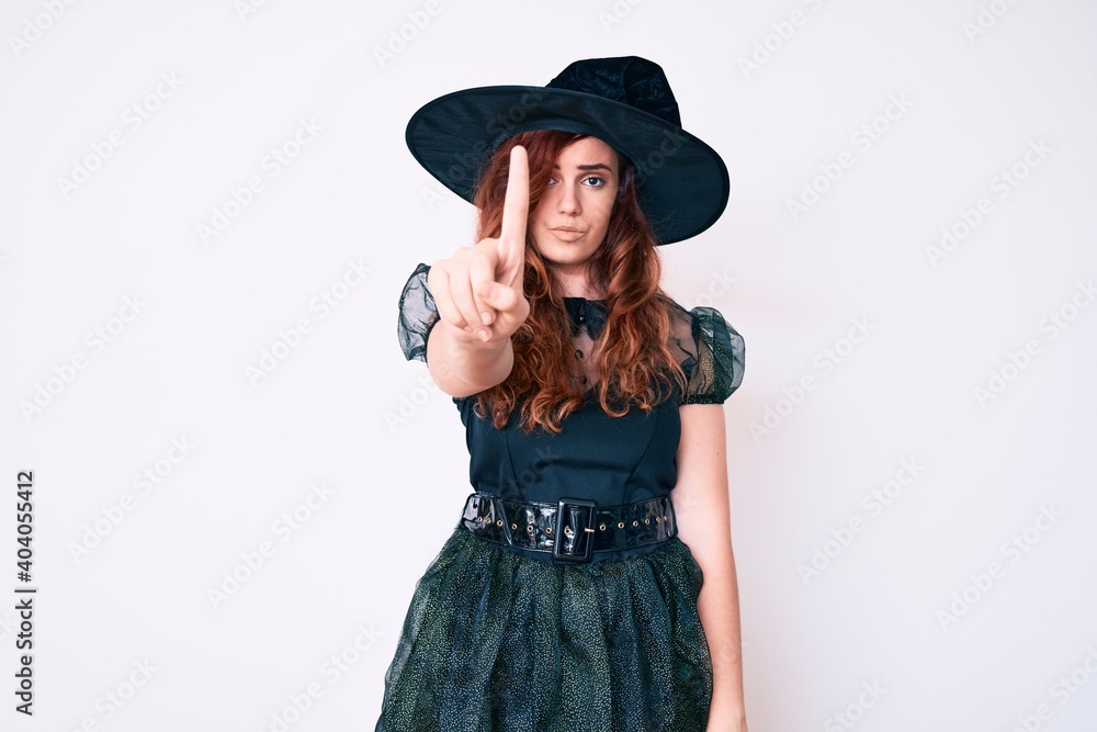 Young beautiful woman wearing witch halloween costume pointing with finger up and angry expression, showing no gesture Young beautiful woman wearing witch halloween costume pointing with finger up and angry expression, showing no gesture