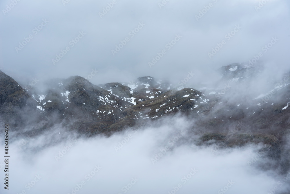 Epic Winter landscape image of view from Side Pike towards Langdale pikes with low level clouds on mountain tops and moody mist swirling around Epic Winter landscape image of view from Side Pike towards Langdale pikes with low level clouds on mountain tops and moody mist swirling around