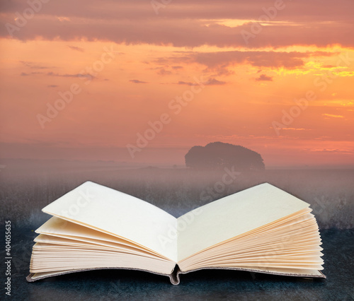Digital composite of Stunning inspirational Summer sunrise landscape image over English countryside with mist hanging in fields in pages of open book