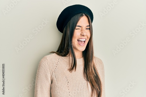 Young brunette woman wearing french look with beret winking looking at the camera with sexy expression, cheerful and happy face.