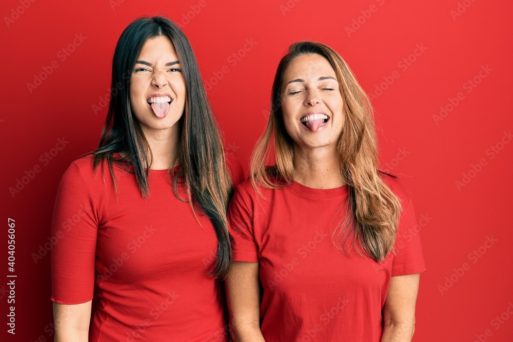 Hispanic family of mother and daughter wearing casual clothes over red background sticking tongue out happy with funny expression. emotion concept. Hispanic family of mother and daughter wearing casual clothes over red background sticking tongue out happy with funny expression. emotion concept.