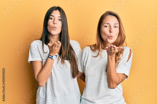 Hispanic family of mother and daughter wearing casual white tshirt looking at the camera blowing a kiss with hand on air being lovely and sexy. love expression.