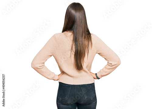Young brunette woman wearing casual winter sweater standing backwards looking away with arms on body