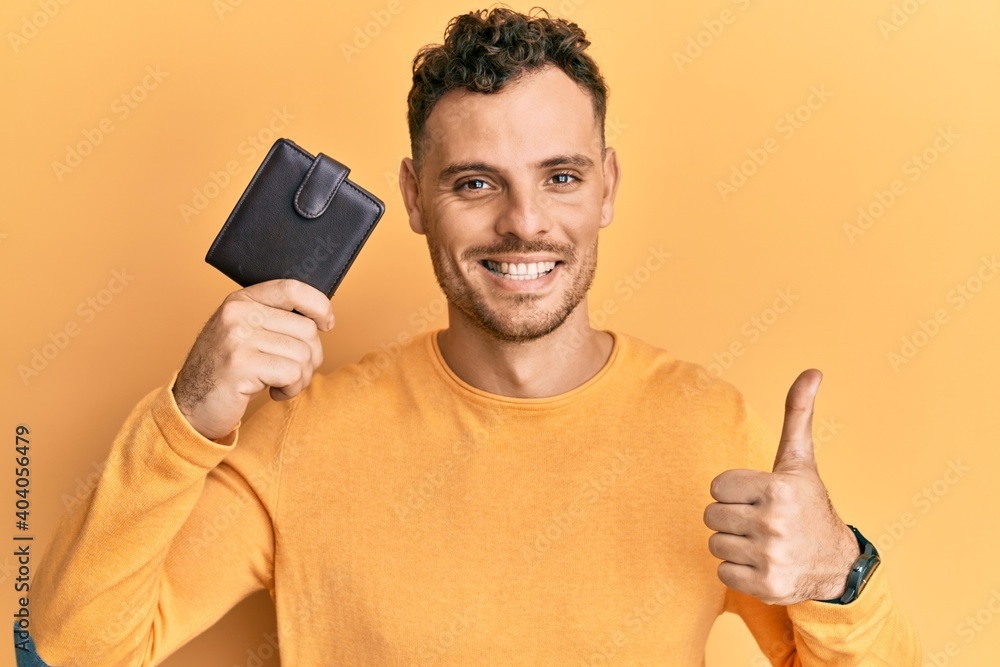 Young hispanic man holding leather wallet smiling happy and positive, thumb up doing excellent and approval sign Young hispanic man holding leather wallet smiling happy and positive, thumb up doing excellent and approval sign
