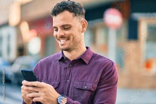 Young hispanic man smiling happy using smartphone at the city.
