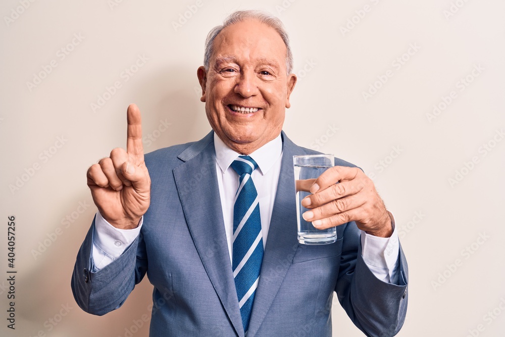 Senior handsome grey-haired businessman wearing suit drinking glass of water to refreshment smiling with an idea or question pointing finger with happy face, number one