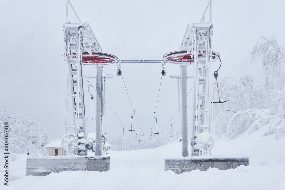upper tower of the ski lift on a snow-covered hilltop among frosty trees