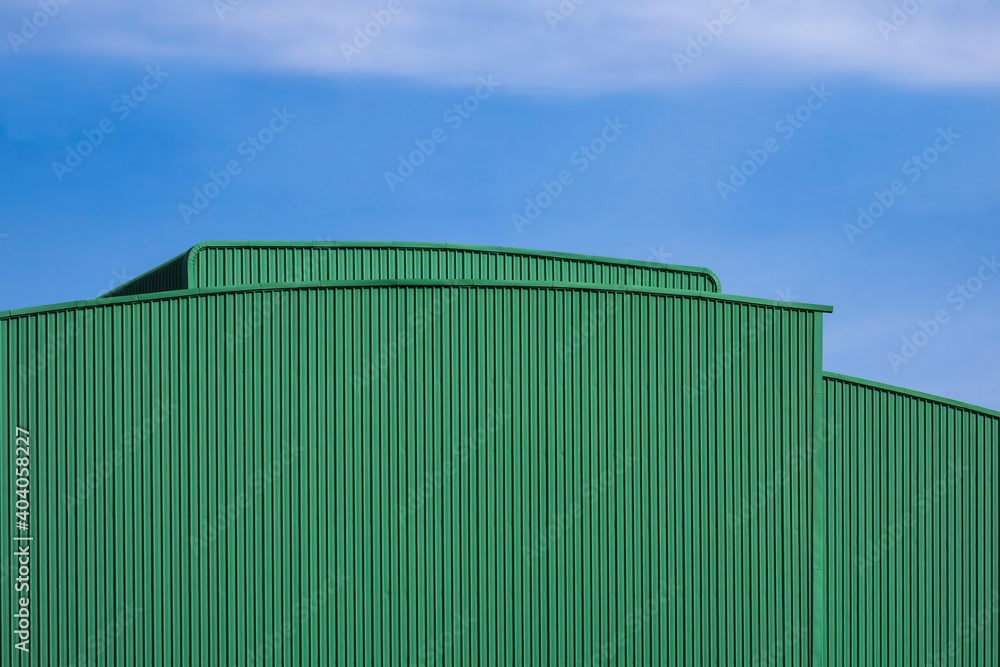 Green corrugated metal warehouse building against blue sky background in perspective view Green corrugated metal warehouse building against blue sky background in perspective view