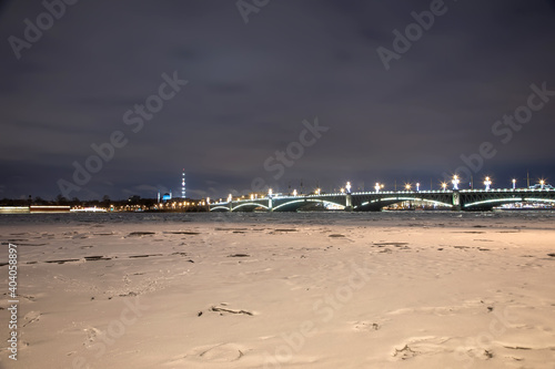 Night bridge over a frozen river and buildings in the distance. Beautiful winter night.