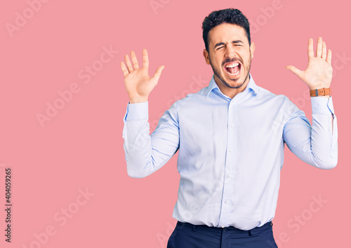 Young hispanic man wearing business clothes celebrating mad and crazy for success with arms raised and closed eyes screaming excited. winner concept © Krakenimages.com